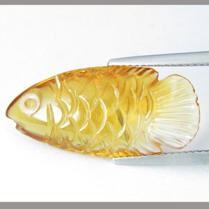 May include: A carved amber fish figurine with a detailed design. The fish is yellow and translucent, with a white fin.