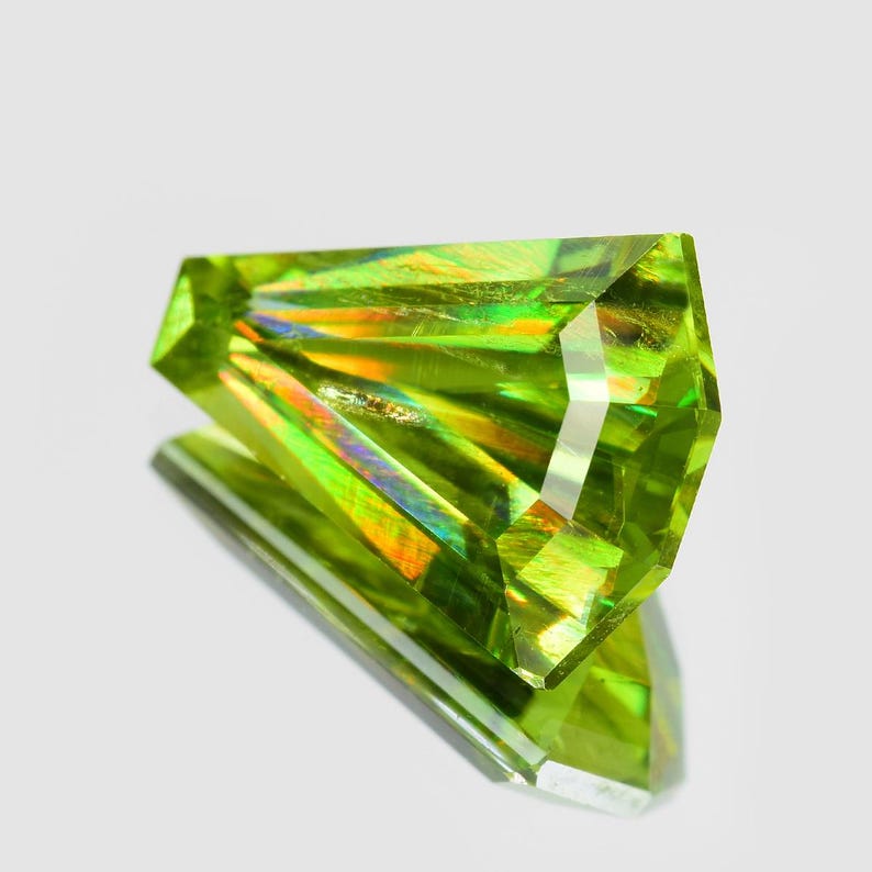 May include: A faceted green gemstone with iridescent rainbow colors. The gemstone is cut into a pointed shape and has a smooth, polished surface.