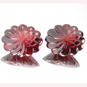 May include: Two red glass candle holders with a flower-shaped design. The holders have a swirl pattern and a clear glass base.