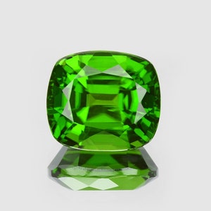 May include: A vibrant green gemstone with a cushion cut. The gem is faceted and has a high level of brilliance.