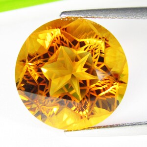 May include: A round, faceted, golden yellow gemstone with a star-shaped pattern inside. The gemstone is held by tweezers.