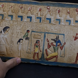 May include: A rectangular stone slab with an ancient Egyptian relief carving. The scene depicts a weighing of the heart ceremony, with Anubis, the jackal-headed god, weighing the heart of a deceased person against a feather. Hieroglyphics are inscribed on the slab.
