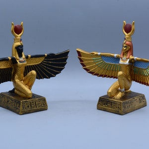 May include: Two gold-painted statues of the Egyptian goddess Isis with outstretched wings. One statue has black wings and the other has gold and blue wings.