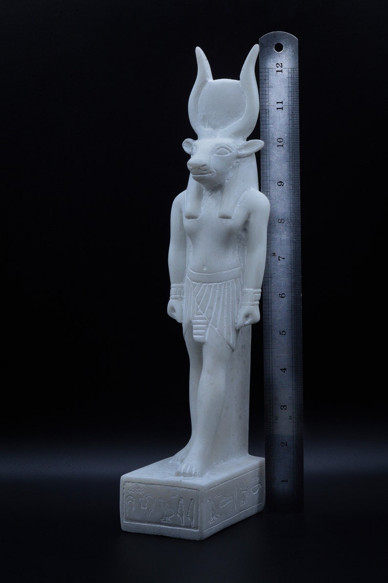 May include: White marble statue of an Egyptian god with a bull's head, wearing a traditional headdress and kilt. The statue is standing on a base with hieroglyphics. The statue is approximately 11 inches tall.