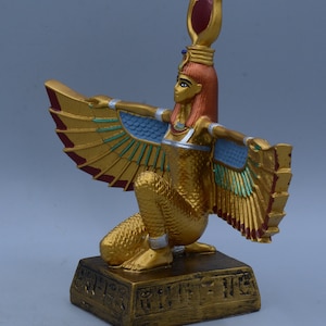 May include: A gold-colored statue of the Egyptian goddess Bastet, depicted as a woman with a cat's head and wings. She is kneeling on a base with hieroglyphics.