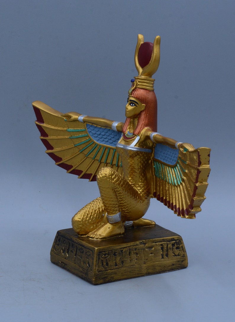 May include: A gold-colored statue of the Egyptian goddess Bastet, depicted as a woman with a cat's head and wings. She is kneeling on a base with hieroglyphics.