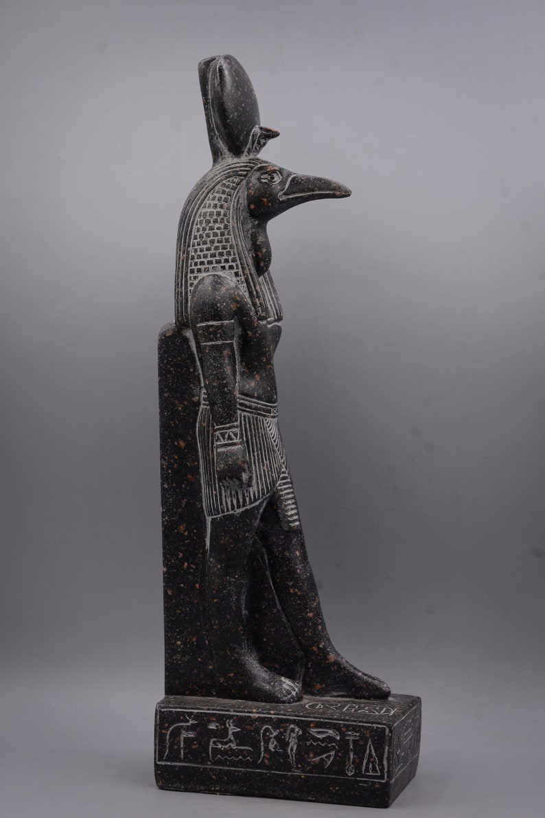 Puede incluir: Estatua de granito negro del dios egipcio Horus, representado como un hombre con cabeza de halc&oacute;n con un cuerpo humano y una cabeza de halc&oacute;n. La estatua est&aacute; de pie sobre una base rectangular con jerogl&iacute;ficos.