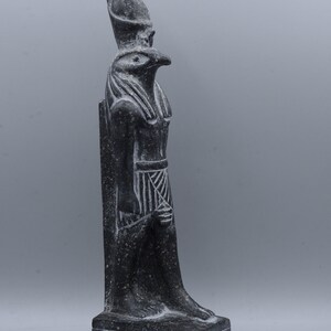 K&ouml;nnte beinhalten: Schwarze Steinstatue des &auml;gyptischen Gottes Horus, dargestellt als falkenk&ouml;pfiger Mann mit einer Doppelkrone. Die Statue steht auf einem Sockel mit Hieroglyphen.