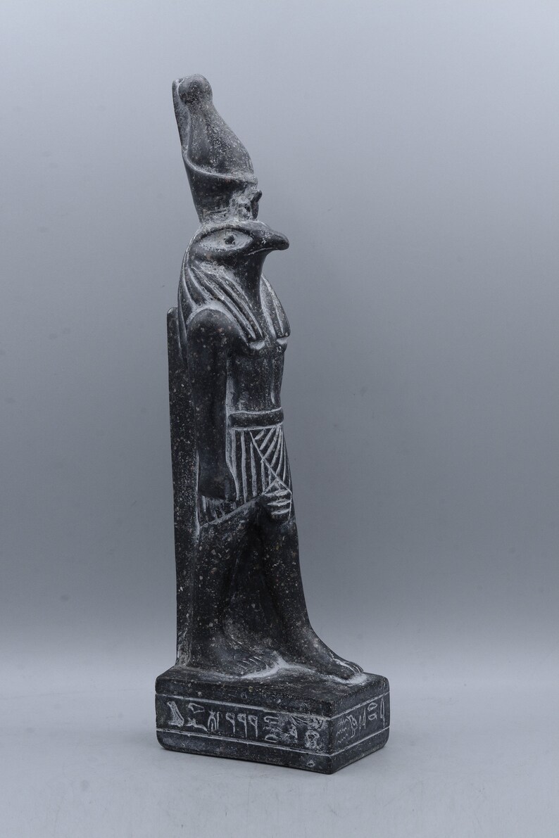 K&ouml;nnte beinhalten: Schwarze Steinstatue des &auml;gyptischen Gottes Horus, dargestellt als falkenk&ouml;pfiger Mann mit einer Doppelkrone. Die Statue steht auf einem Sockel mit Hieroglyphen.