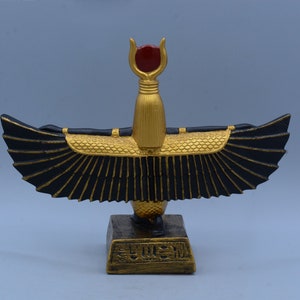 May include: A gold and black statue of the Egyptian goddess Bastet, with outstretched wings and a red gem on her head. The statue is on a base with hieroglyphics.