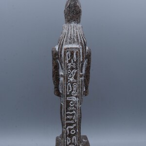 K&ouml;nnte beinhalten: Eine braune Granitstatue eines &auml;gyptischen Gottes mit Hieroglyphen, die auf die Vorderseite geschnitzt sind. Die Statue steht auf einem rechteckigen Sockel.