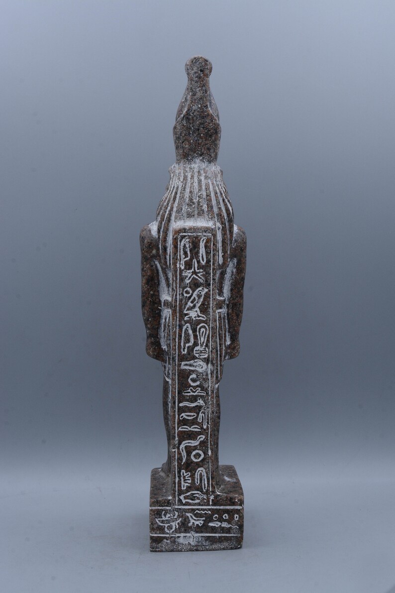 K&ouml;nnte beinhalten: Eine braune Granitstatue eines &auml;gyptischen Gottes mit Hieroglyphen, die auf die Vorderseite geschnitzt sind. Die Statue steht auf einem rechteckigen Sockel.