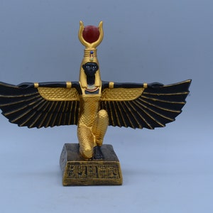 May include: A gold and black figurine of the Egyptian goddess Bastet, with outstretched wings and a red gem on her headdress. She is kneeling on a base with hieroglyphics.