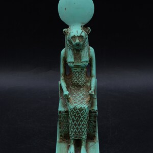Peut inclure: Statue turquoise d'une divinit&eacute; &eacute;gyptienne, peut-&ecirc;tre Sekhmet, assise sur un tr&ocirc;ne. La figure a une t&ecirc;te de lionne, un disque solaire et des d&eacute;tails complexes sur la robe et le tr&ocirc;ne. La statue mesure environ 15 cm de haut.