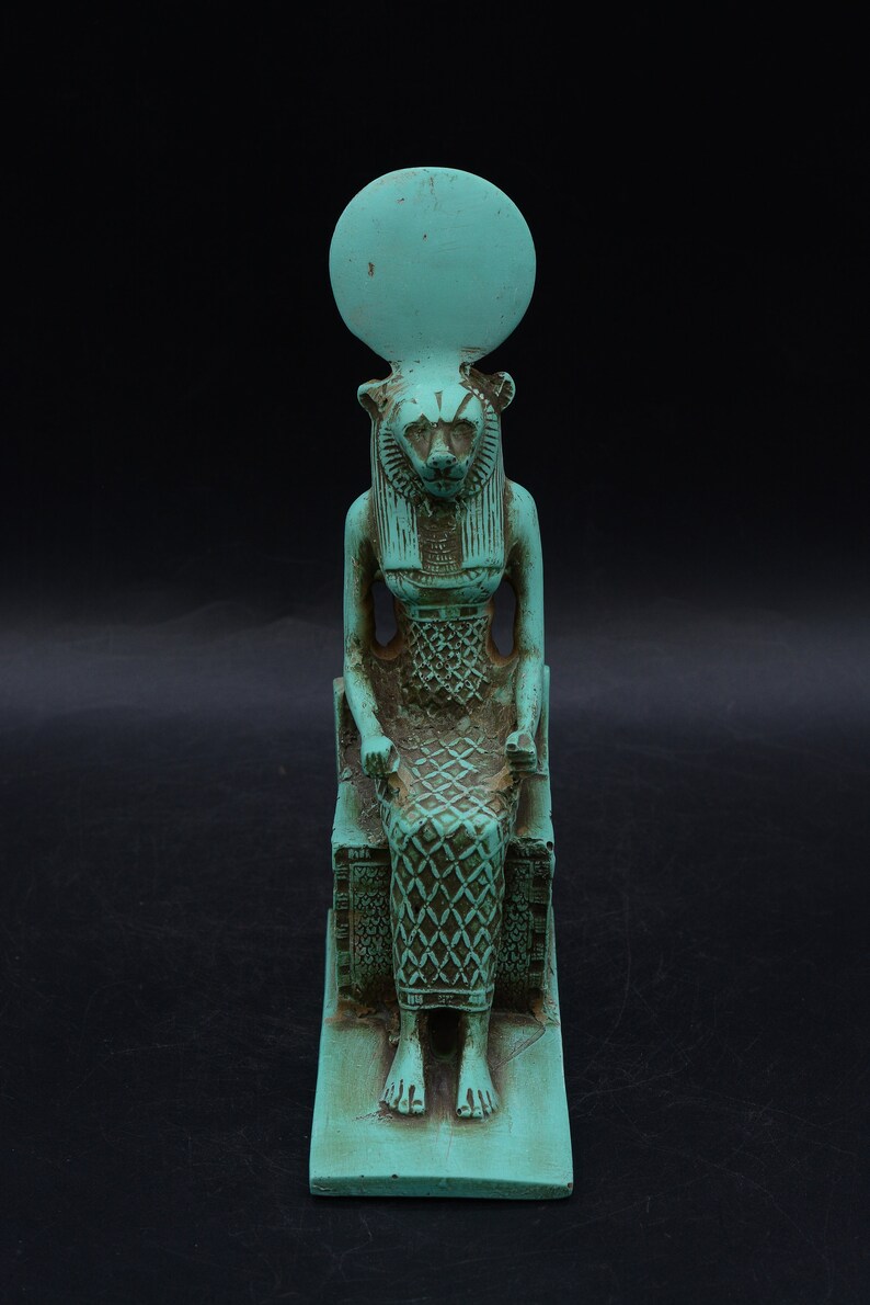 Peut inclure: Statue turquoise d'une divinit&eacute; &eacute;gyptienne, peut-&ecirc;tre Sekhmet, assise sur un tr&ocirc;ne. La figure a une t&ecirc;te de lionne, un disque solaire et des d&eacute;tails complexes sur la robe et le tr&ocirc;ne. La statue mesure environ 15 cm de haut.