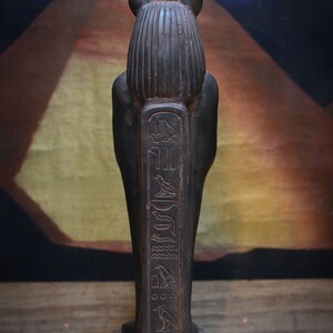 以下が含まれることがあります： ジャッカルの頭をつけたエジプトの神の黒い木製の像。像は台座の上に立っており、正面にヒエログリフが刻まれています。