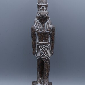 K&ouml;nnte beinhalten: Eine braune Granitstatue eines &auml;gyptischen Gottes mit einem menschlichen K&ouml;rper und einem Froschkopf. Der Gott tr&auml;gt eine traditionelle &auml;gyptische Kopfbedeckung und einen Rock. Die Statue steht auf einem Sockel mit Hieroglyphen.