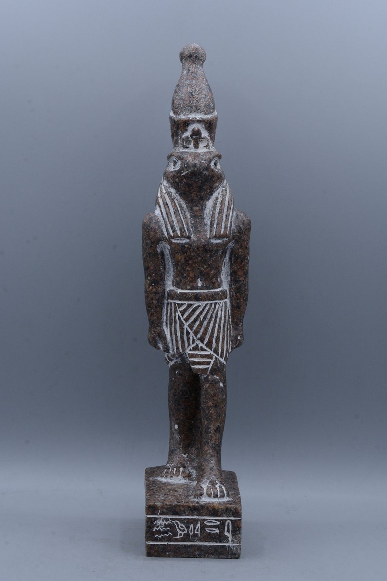 K&ouml;nnte beinhalten: Eine braune Granitstatue eines &auml;gyptischen Gottes mit einem menschlichen K&ouml;rper und einem Froschkopf. Der Gott tr&auml;gt eine traditionelle &auml;gyptische Kopfbedeckung und einen Rock. Die Statue steht auf einem Sockel mit Hieroglyphen.