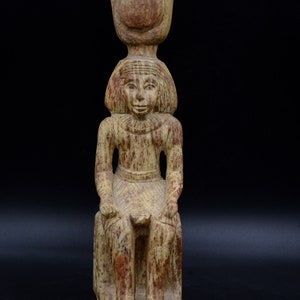 May include: A seated statue of an Egyptian deity with a crown and a headdress. The statue is made of a light brown stone with a weathered finish.