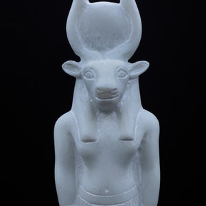 May include: White figurine of an Egyptian god with a bull's head and horns. The god is wearing a traditional Egyptian headdress and a kilt.