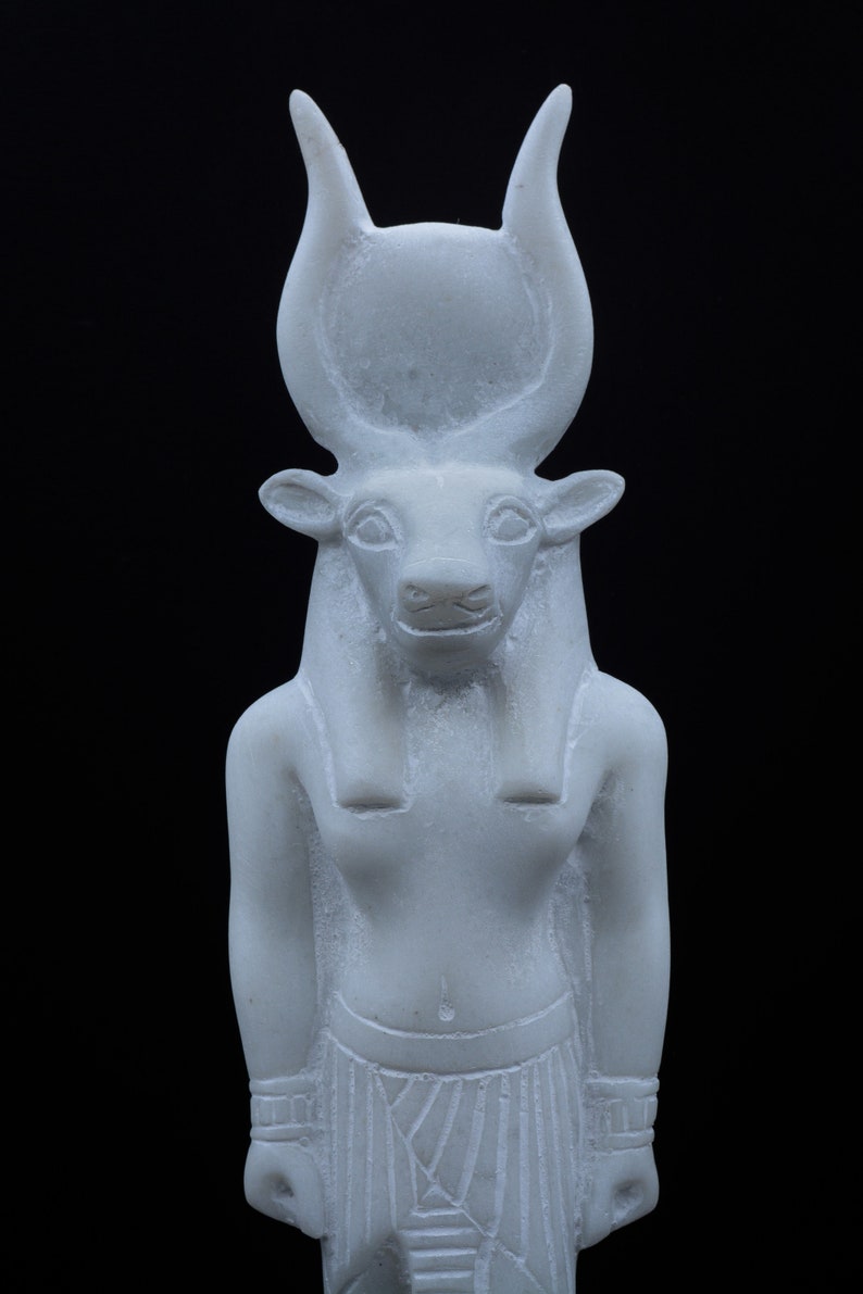 May include: White figurine of an Egyptian god with a bull's head and horns. The god is wearing a traditional Egyptian headdress and a kilt.