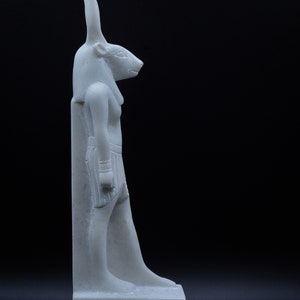 May include: White marble statue of an Egyptian god with a jackal head, standing on a base with hieroglyphics.