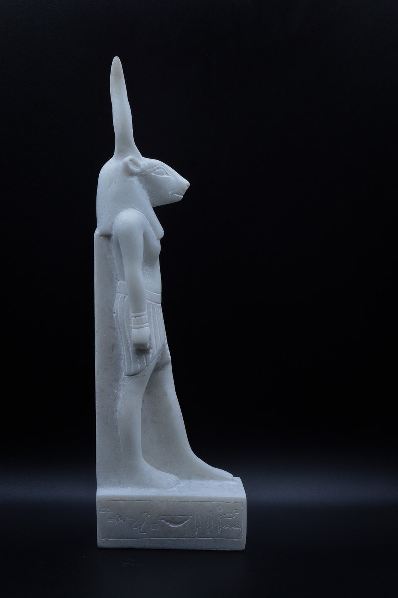 May include: White marble statue of an Egyptian god with a jackal head, standing on a base with hieroglyphics.