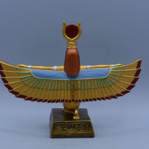 May include: Gold winged statue of the Egyptian goddess Isis with a red crown and a blue and green patterned body. The statue is standing on a gold base with hieroglyphics.