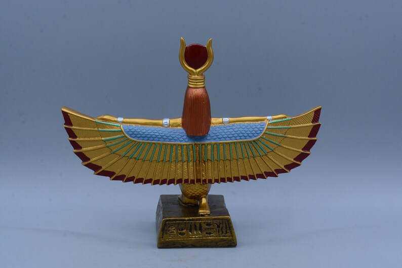 May include: Gold winged statue of the Egyptian goddess Isis with a red crown and a blue and green patterned body. The statue is standing on a gold base with hieroglyphics.