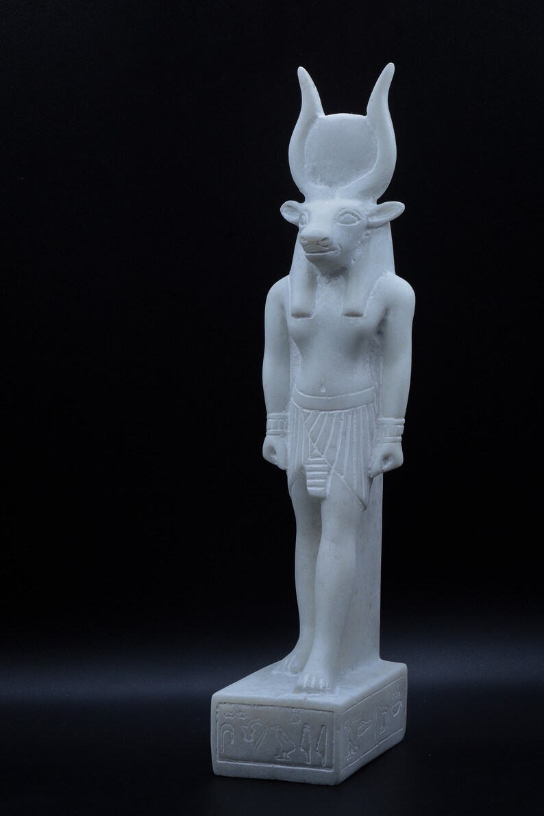 May include: White marble statue of an Egyptian god with a bull's head, wearing a headdress and a kilt. The statue is standing on a base with hieroglyphs.