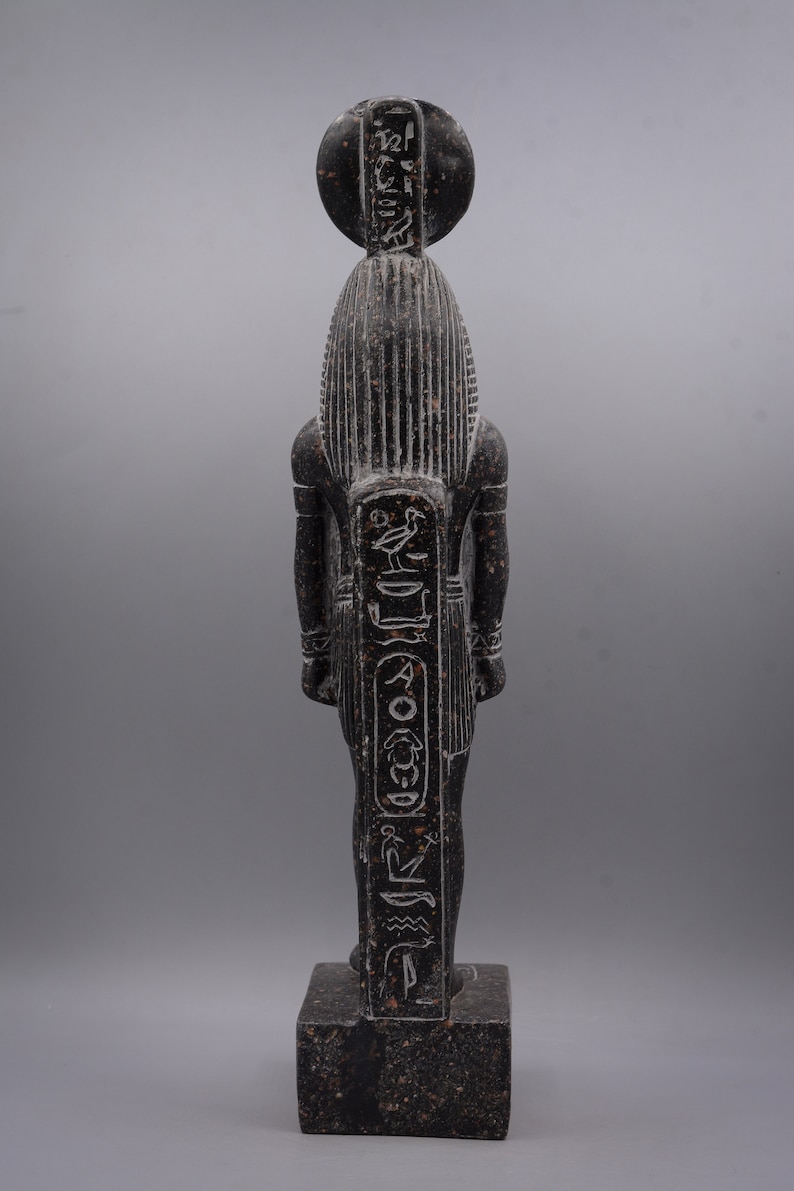Puede incluir: Estatua de un dios egipcio de granito negro con jerogl&iacute;ficos en la parte delantera y trasera. La estatua est&aacute; de pie sobre una base cuadrada.
