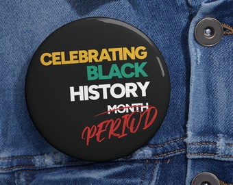 May include: A black button with the text "CELEBRATING BLACK HISTORY MONTH PERIOD" in yellow, green, white, and red. The button is set against a denim jacket.
