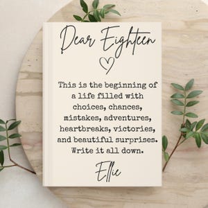 May include: A cream-colored journal with black text that reads: Dear Eighteen, followed by a heart icon, and the text: This is the beginning of a life filled with choices, chances, mistakes, adventures, heartbreaks, victories, and beautiful surprises. Write it all down. Ellie.