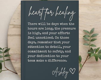 May include: A dark gray rectangular journal with white text that reads: heart for healing. There will be days when the hours are long, the pressure is high, and your efforts feel unnoticed. On those days, remember that your attention to detail, your commitment to safety, and your dedication to your team make a difference. Ashley with a heart symbol.