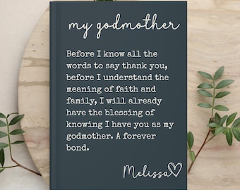 May include: A dark gray hardcover book with white text that reads: my godmother. Before I know all the words to say thank you, before I understand the meaning of faith and family, I will already have the blessing of knowing I have you as my godmother. A forever bond. Melissa with a heart symbol.