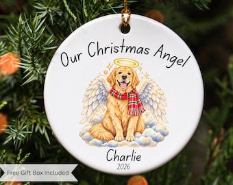 May include: A round white ceramic Christmas ornament featuring a golden retriever with angel wings and a halo, wearing a red and green plaid scarf. The text reads Our Christmas Angel, Charlie, and 2026. It hangs from a gold string.