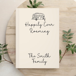 May include: A cream-colored hardcover book featuring a black line drawing of a vintage camper trailer at the top. Below the illustration, the text reads "Happily Ever Roaming" and "The Smith Family" in a simple black script font.