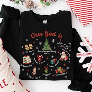 以下が含まれることがあります： 赤色の「Our God Is」という文字が入った黒いクルーネックのスウェットシャツ。デザインにはクリスマスツリー、ジンジャーブレッドマン、サンタクロース、その他のホリデーをテーマにしたグラフィックが含まれています。スウェットシャツはクラシックなフィット感です。