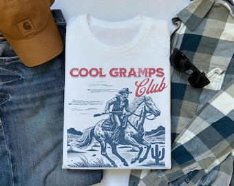 May include: White t-shirt with a blue and red graphic of a cowboy riding a horse. The graphic says "Cool Gramps Club".