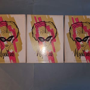 May include: Three vintage boxes with a woman's face wearing a black mask and the word "Mystere" printed on each box. The boxes are yellow with pink accents.