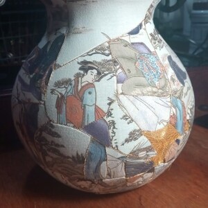 May include: A ceramic vase with a white background and a patchwork design of various scenes featuring people, trees, and flowers. The vase is decorated with gold accents and has a round shape.
