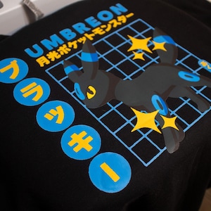 May include: Black t-shirt with a blue and yellow graphic of a Pokemon character, Umbreon, with the text "UMBREON 月光ポケモンマスター" in Japanese.