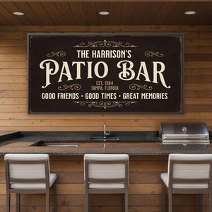 May include: A dark brown sign with the text "THE HARRISON'S PATIO BAR" in a decorative font. Below, it reads "EST. 1984 TAMPA, FLORIDA" and "GOOD FRIENDS • GOOD TIMES • GREAT MEMORIES". The sign is mounted above a bar with stools.
