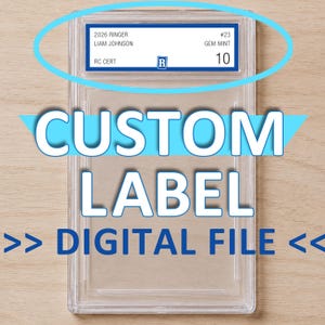 以下が含まれることがあります： 上部に青い縁取りの白いラベルが付いた、トレーディングカード用の透明な長方形のプラスチック製保護ケース。ラベルには「2026 RINGER」「LIAM JOHNSON」「#23」「GEM MINT 10」「RC CERT」という文字と、中央に青い「R」のロゴが記載されています。