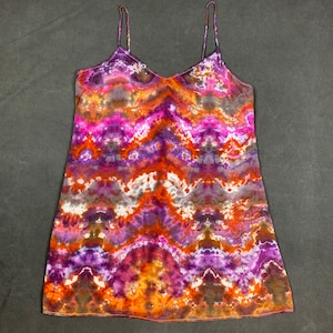 May include: A tie-dye slip dress with a V-neck and thin straps. The dress is a mix of purple, orange, and brown colors.