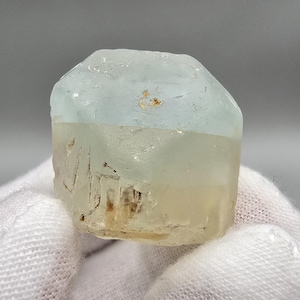 Peut inclure: Une pierre précieuse brute et non taillée, avec un dégradé de couleurs bleu clair et jaune pâle. La partie supérieure est d'un bleu clair translucide, passant à un jaune pâle à la base. La pierre a une texture brute et naturelle.