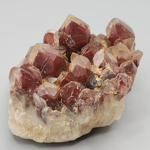 May include: A cluster of red and clear quartz crystals. The crystals are clustered together in a natural formation. The crystals are translucent and have a glassy lustre.