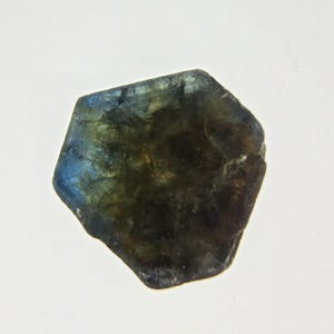 May include: A polished, irregularly shaped gemstone with a mix of dark green, blue, and brown hues. The stone has a translucent quality, with light reflecting off its surface. The edges are slightly rounded, and the overall shape is reminiscent of a flattened pebble.