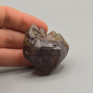 May include: A dark brown crystal cluster with a faceted, geometric shape and a rough, textured surface. The crystal has multiple points and facets, and it appears to be a natural mineral specimen. The crystal is held in a hand.