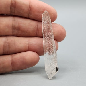 May include: A clear quartz crystal point with a black inclusion. The crystal is approximately 5 cm long and has a pointed tip.